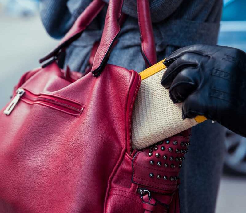 Someone stealing a woman's wallet from her pink purse.