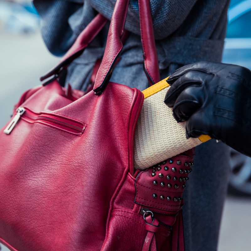 Someone stealing a woman's wallet from her pink purse.